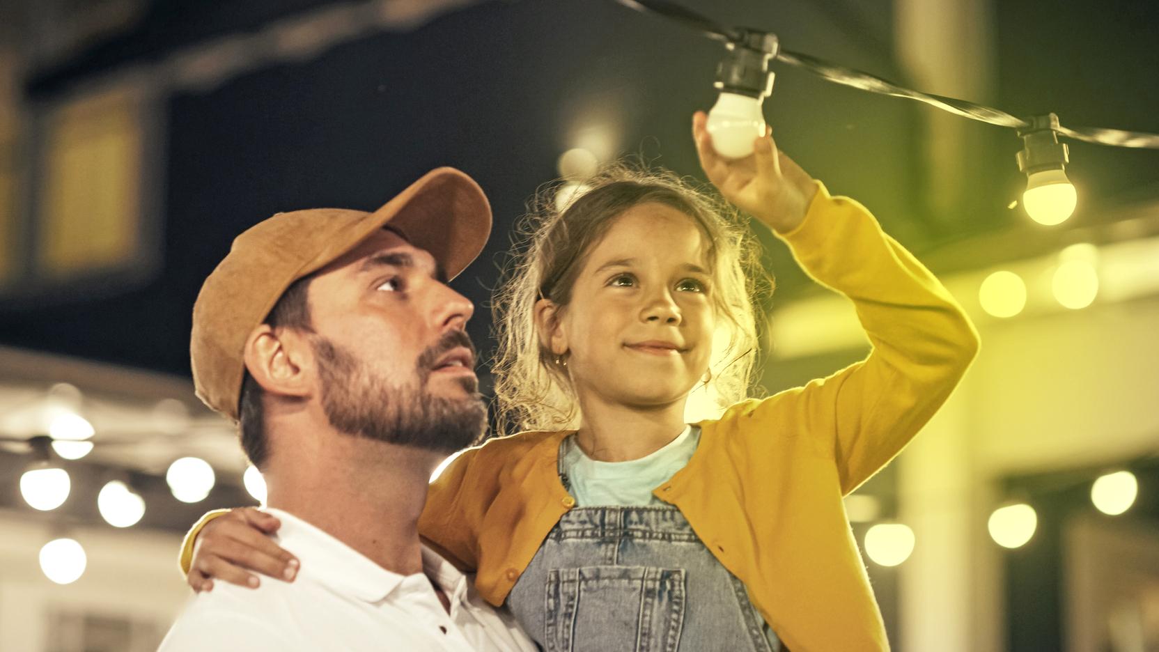 Ein Mann hat ein Mädchen auf dem Arm, das auf eine Lichterkette zeigt
