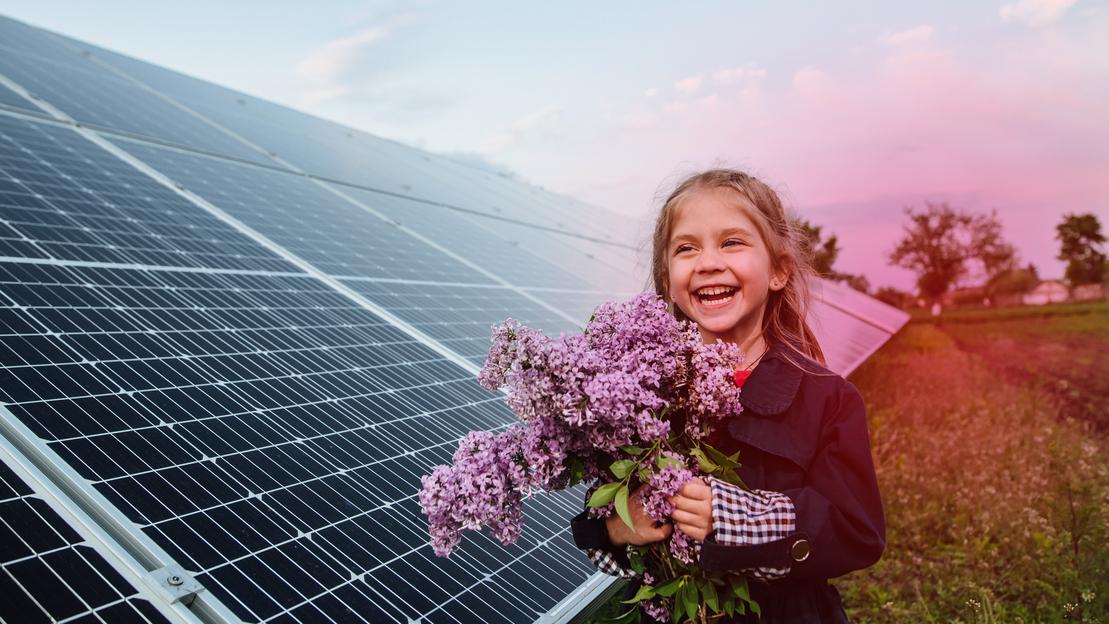 Ein M&auml;dchen steht vor einem Solarpark mit mehreren PV-Modulen