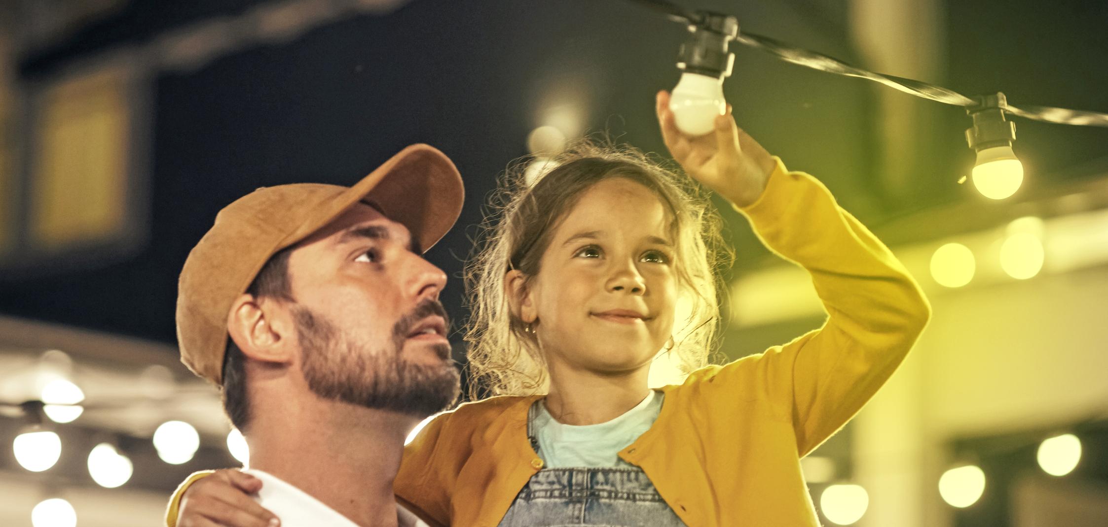 Ein Mann hat ein Mädchen auf dem Arm, das auf eine Lichterkette zeigt Ein Mann hat ein Mädchen auf dem Arm, das auf eine Lichterkette zeigt