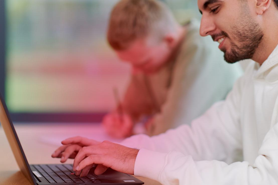 Zwei junge Männer sitzen an einem Schreibtisch und haben einen Laptop vor sich Zwei junge Männer sitzen an einem Schreibtisch und haben einen Laptop vor sich