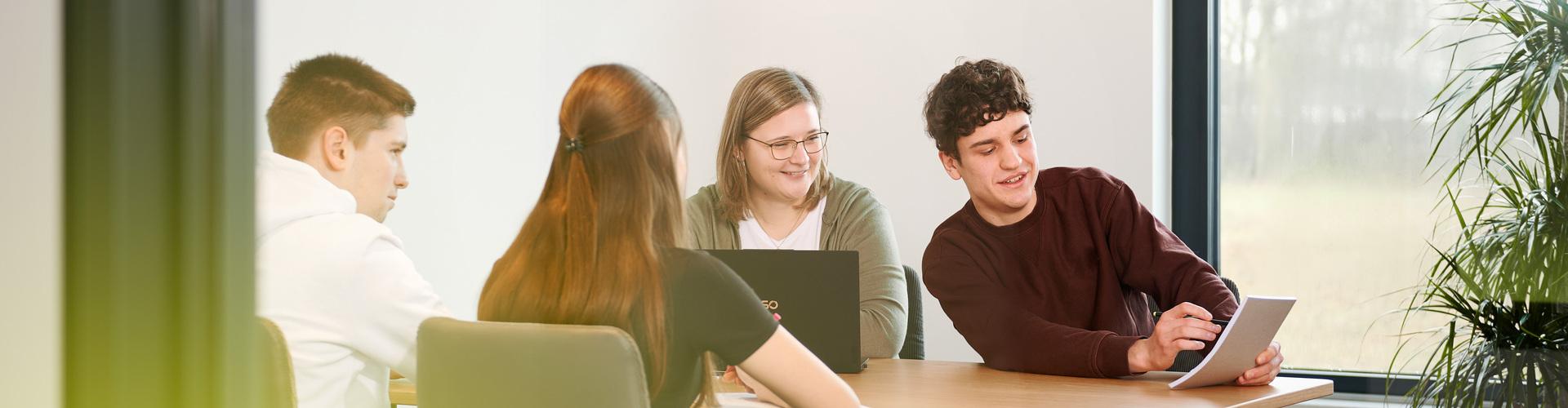 Vier junge Menschen sitzen an einem Besprechungstisch und arbeiten