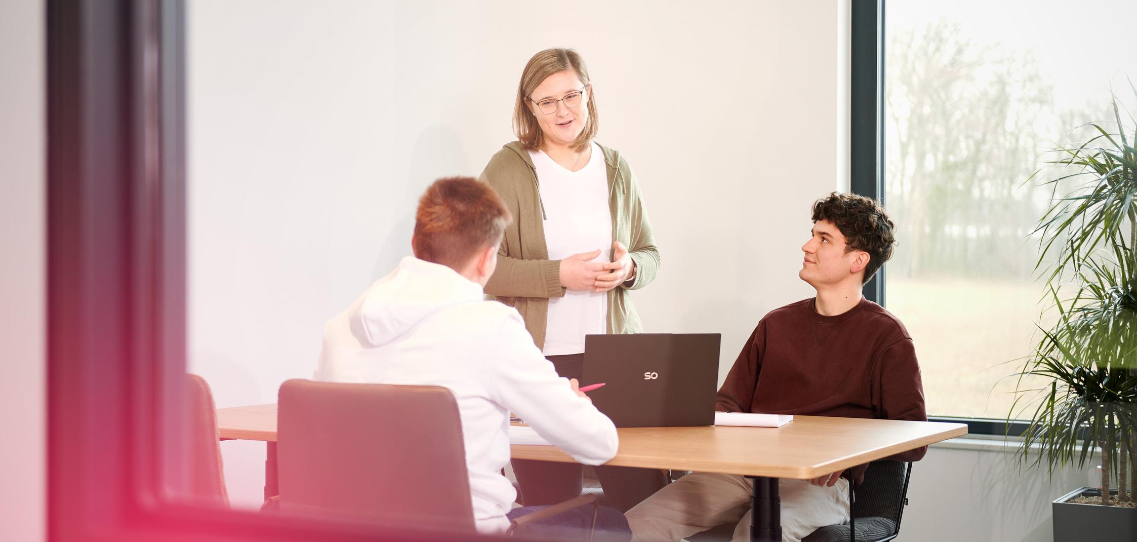 Drei junge Menschen sitzen an einem Besprechungstisch und arbeiten