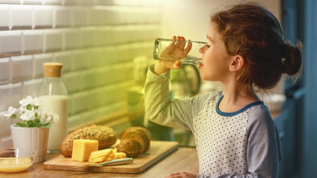 Ein Kind steht in der K&uuml;che und trinkt ein Glas Wasser