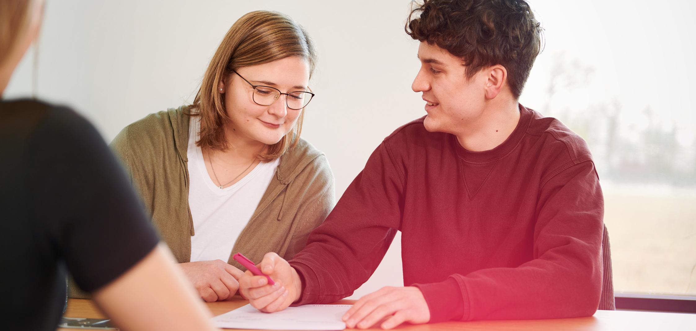 Eine junge Frau schaut einem jungen Mann über die Schulter