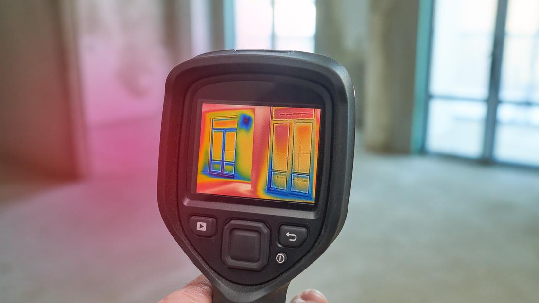 Eine Wärmebildkamera ist auf ein Haus gerichtet und zeigt Wärmeverluste
