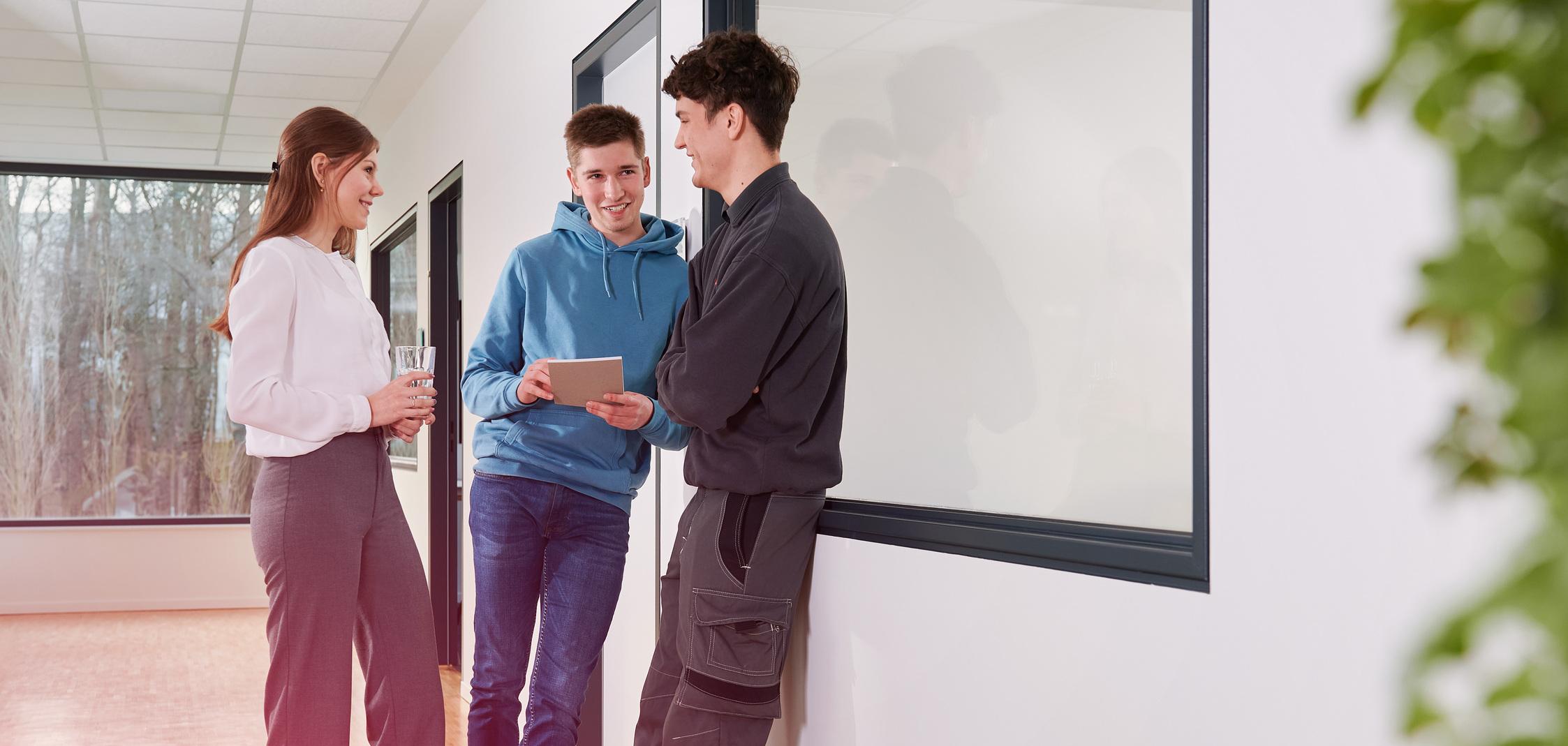 Zwei junge Männer und eine junge Frau stehen in einem Flur und unterhalten sich Zwei junge Männer und eine junge Frau stehen in einem Flur und unterhalten sich