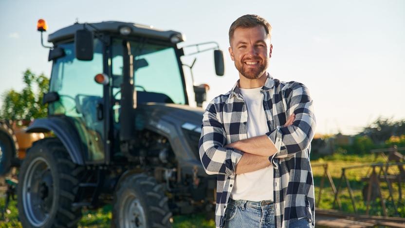 Ein junger Landwirt mit einem karierten Hemd vor einem Traktor Ein junger Landwirt mit einem karierten Hemd vor einem Traktor