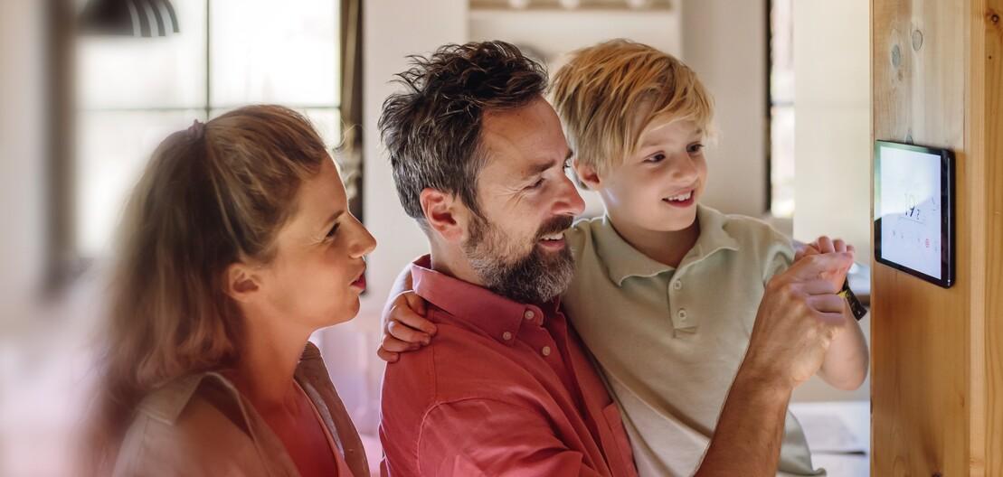 Ein Frau und ein Mann mit einem Kind auf dem Arm stellen die Temperatur an einem Smart Home-Regler ein