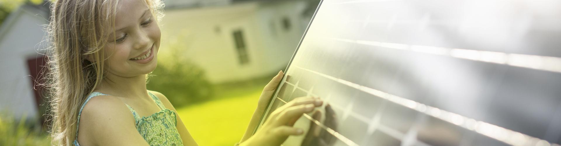 Ein Mädchen steht vor einem Photovoltaik-Modul und schaut es an