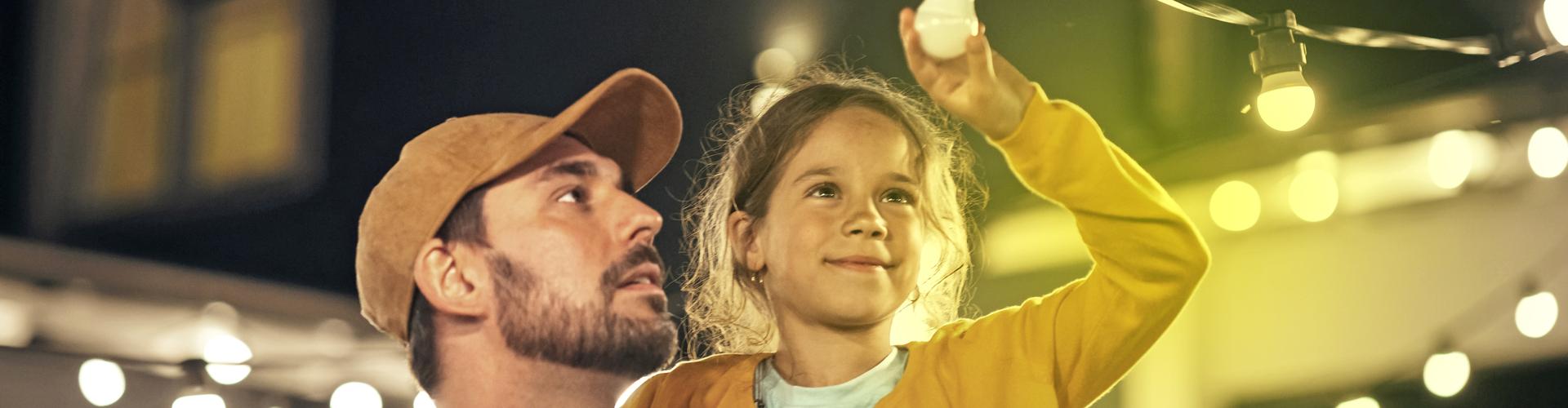 Ein Mann hat ein M&auml;dchen auf dem Arm, das auf eine Lichterkette zeigt