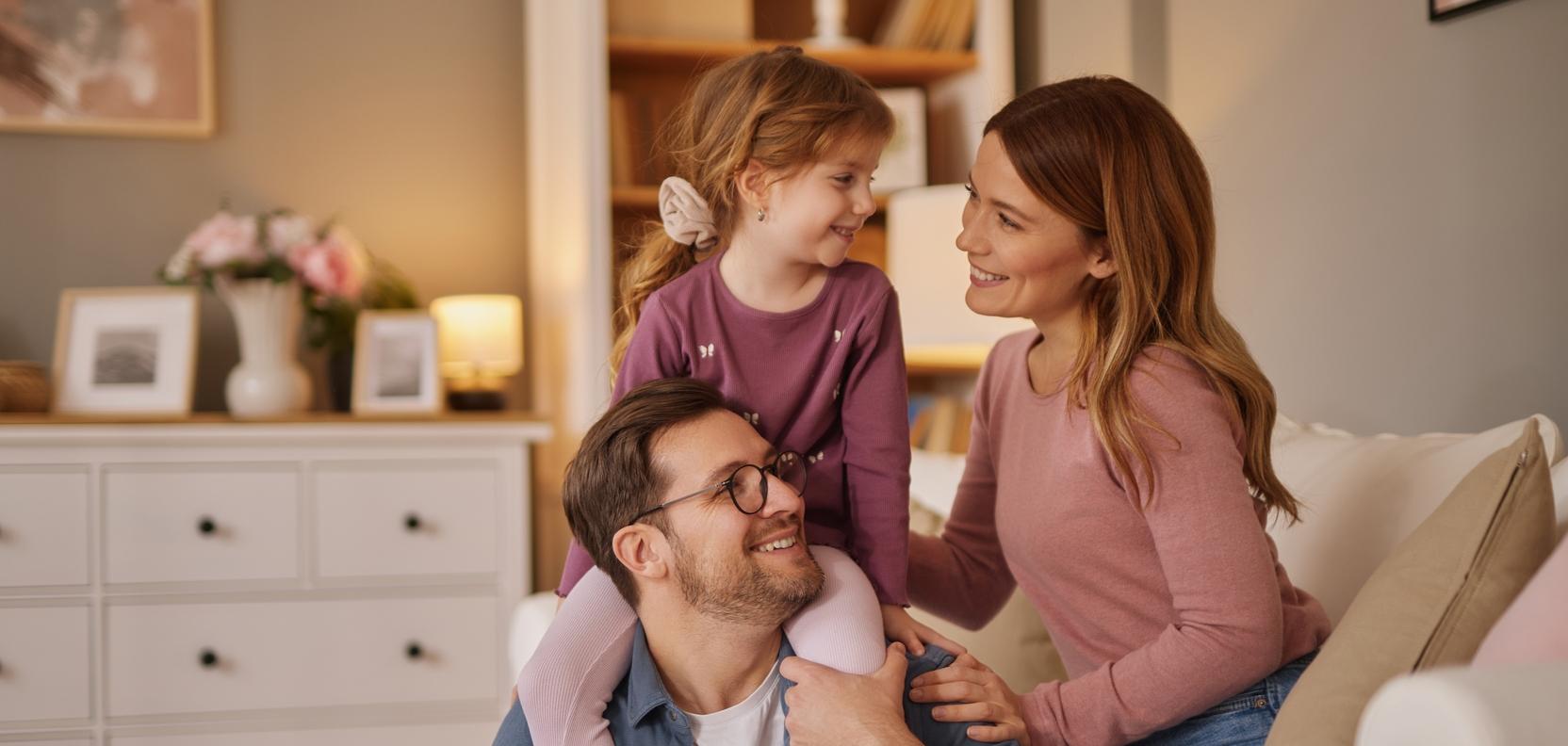 Eine Frau und ein Mann sitzen auf dem Sofa und kuscheln mit einem kleinen Mädchen Eine Frau und ein Mann sitzen auf dem Sofa und kuscheln mit einem kleinen Mädchen