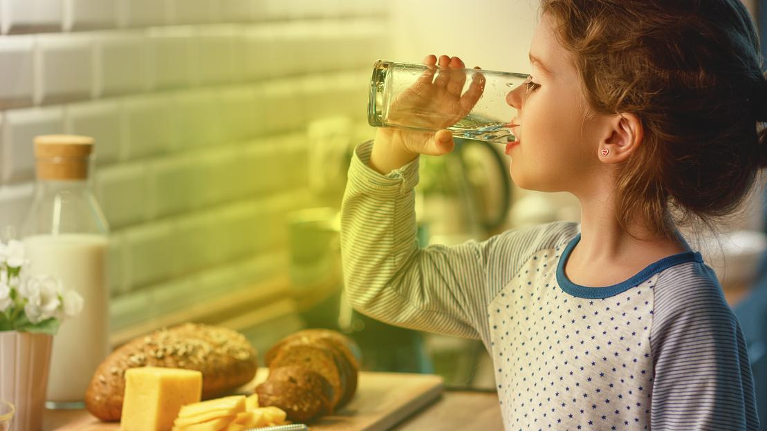 Ein Kind steht in der Küche und trinkt ein Glas Wasser