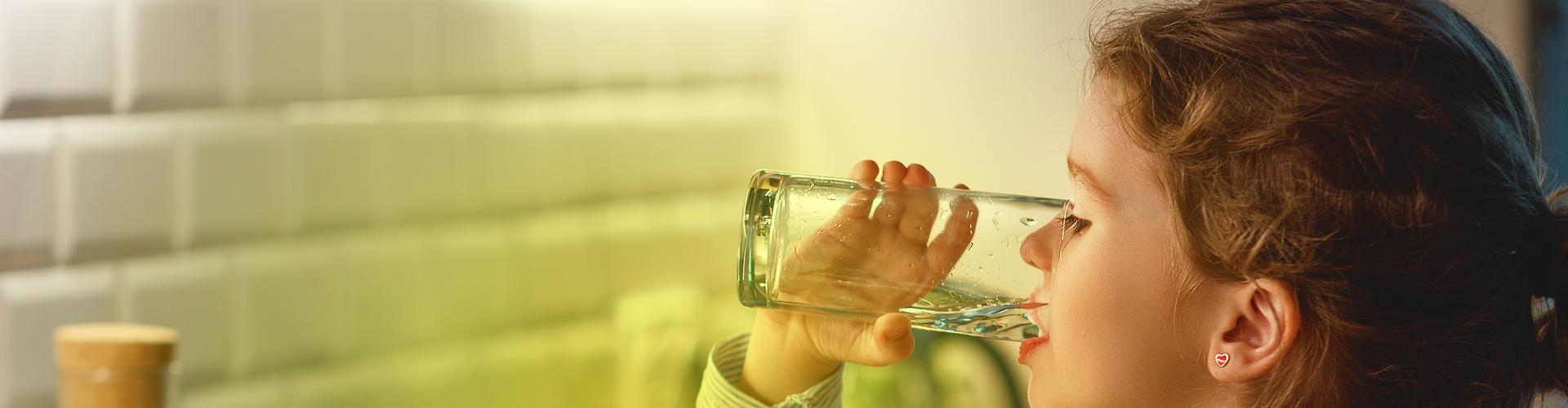 Ein Kind steht in der Küche und trinkt ein Glas Wasser