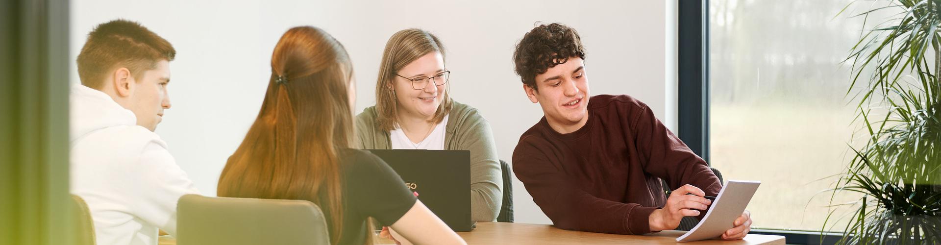 Vier junge Menschen sitzen an einem Besprechungstisch und arbeiten