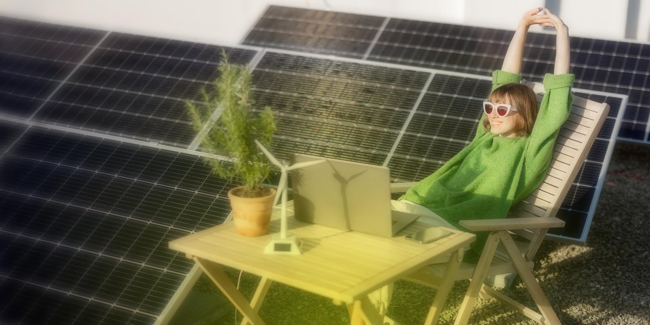 Eine Frau sitzt entspannt auf einem Liegestuhl neben PV-Modulen