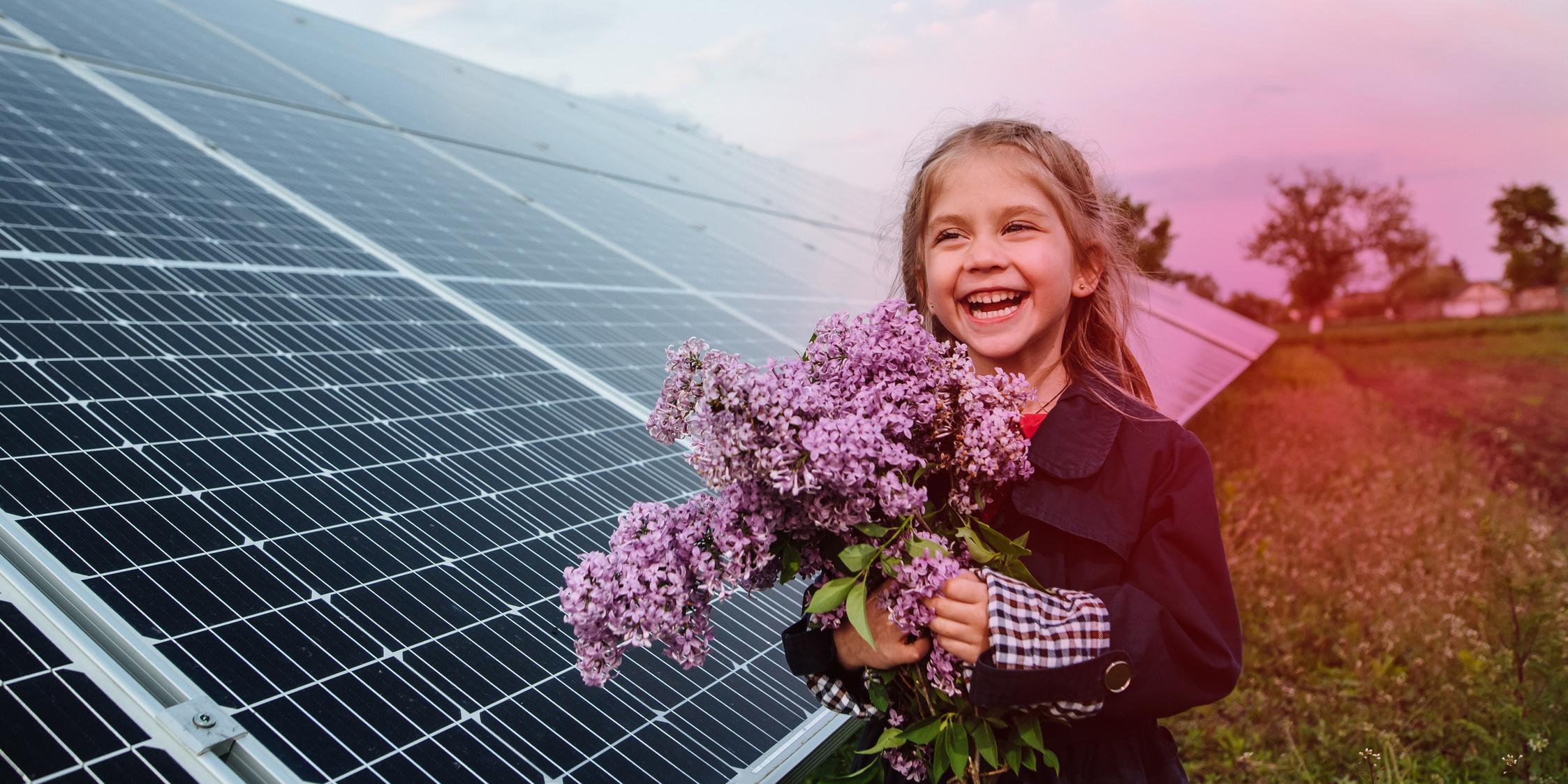 Ein Mädchen steht vor einem Solarpark mit mehreren PV-Modulen