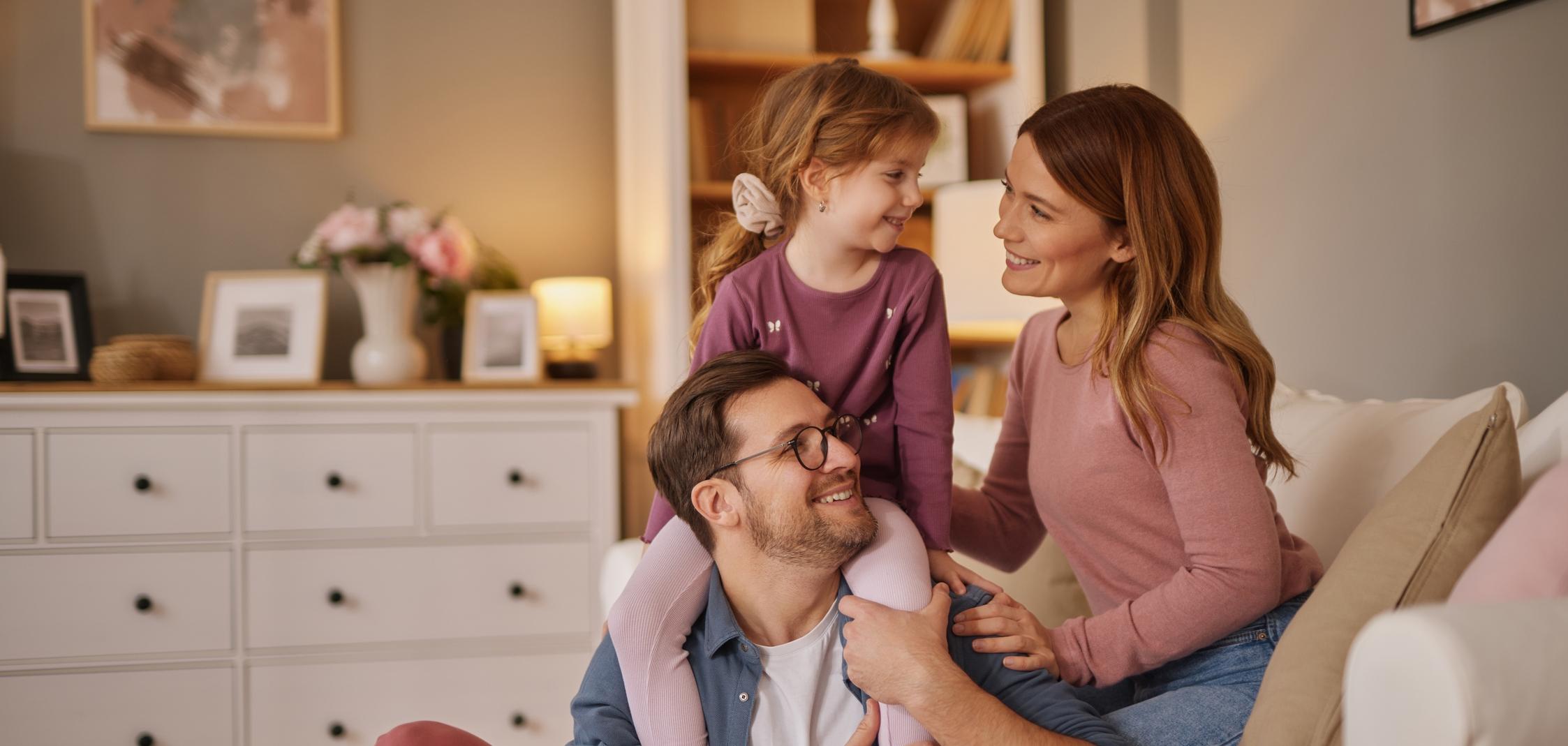 Eine Frau und ein Mann sitzen auf dem Sofa und kuscheln mit einem kleinen Mädchen Eine Frau und ein Mann sitzen auf dem Sofa und kuscheln mit einem kleinen Mädchen