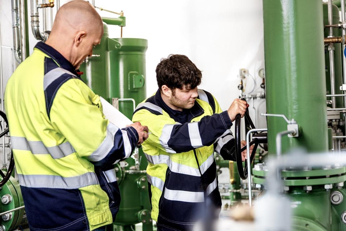 Zwei Mitarbeiter der Stadtwerke Ostm&uuml;nsterland kontrollieren und bedienen eine gr&uuml;ne Industrieanlage