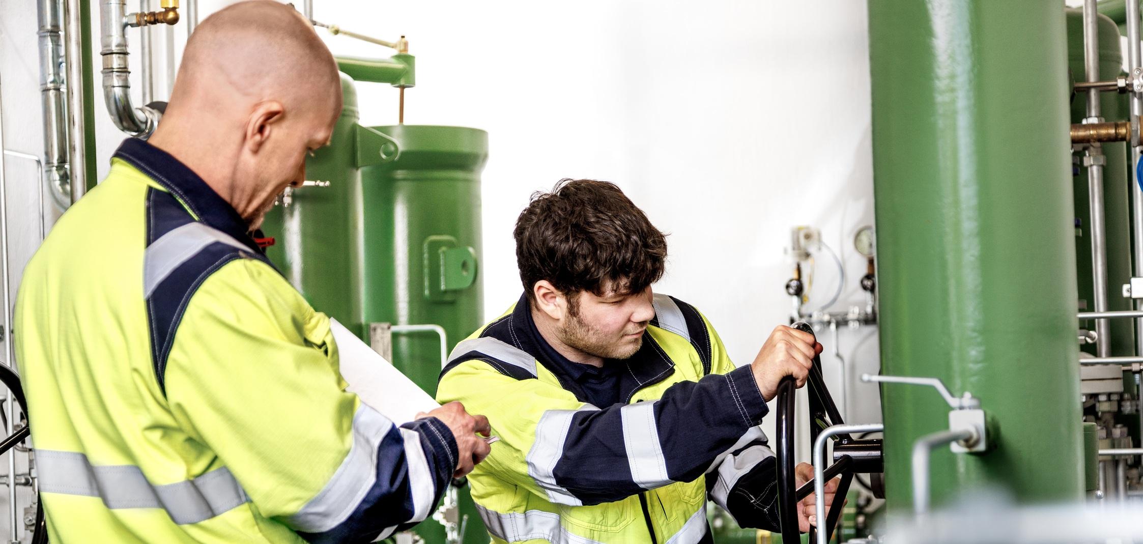 Zwei Mitarbeiter der Stadtwerke Ostmünsterland kontrollieren und bedienen eine grüne Gasdruckanlage Zwei Mitarbeiter der Stadtwerke Ostmünsterland kontrollieren und bedienen eine grüne Industrieanlage