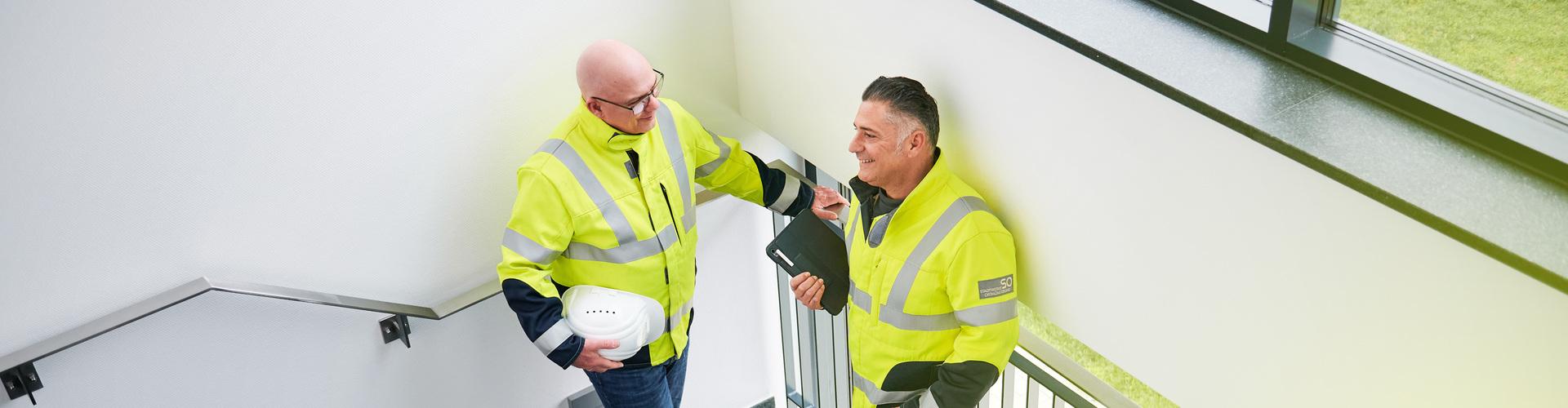 Zwei Elektriker der Stadtwerke Ostmünsterland unterhalten sich im Treppenhaus Zwei Elektriker der Stadtwerke Ostmünsterland unterhalten sich im Treppenhaus