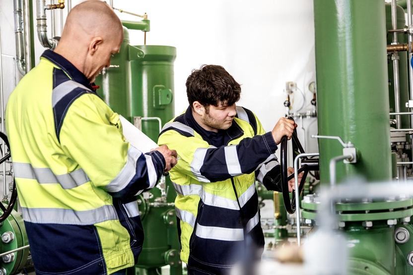 Zwei Mitarbeiter der Stadtwerke Ostm&uuml;nsterland kontrollieren und bedienen eine gr&uuml;ne Industrieanlage