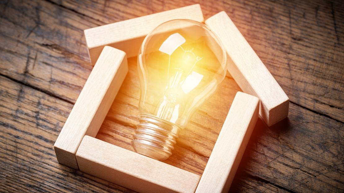 Holzhaus mit Glühbirne Holzstücke bilden ein Haus, darin befindet sich eine Glühbirne.