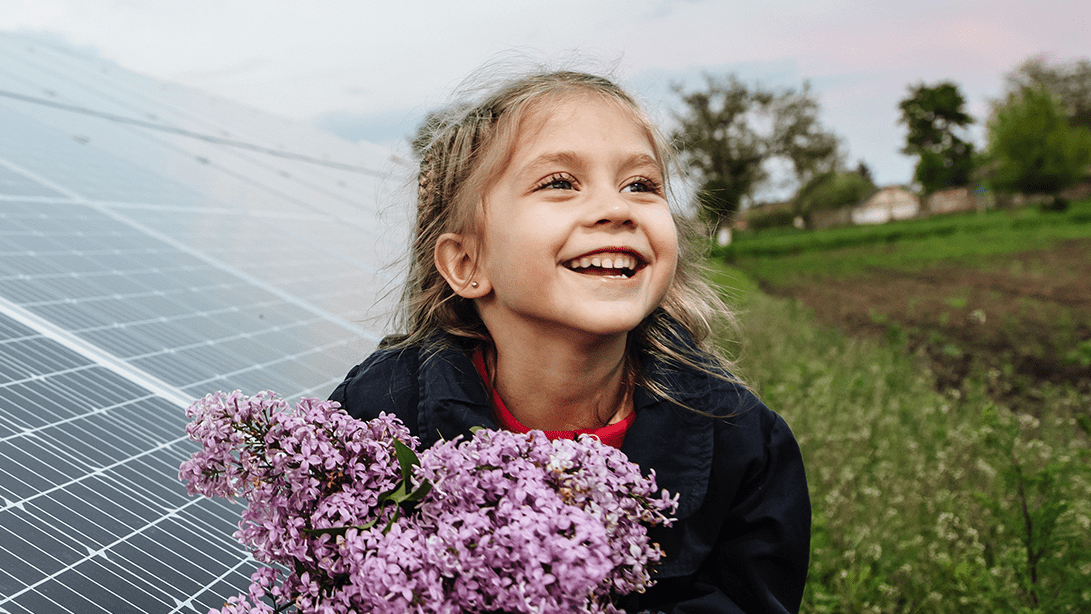 Ein Mädchen steht vor einem Solarpark mit mehreren PV-Modulen