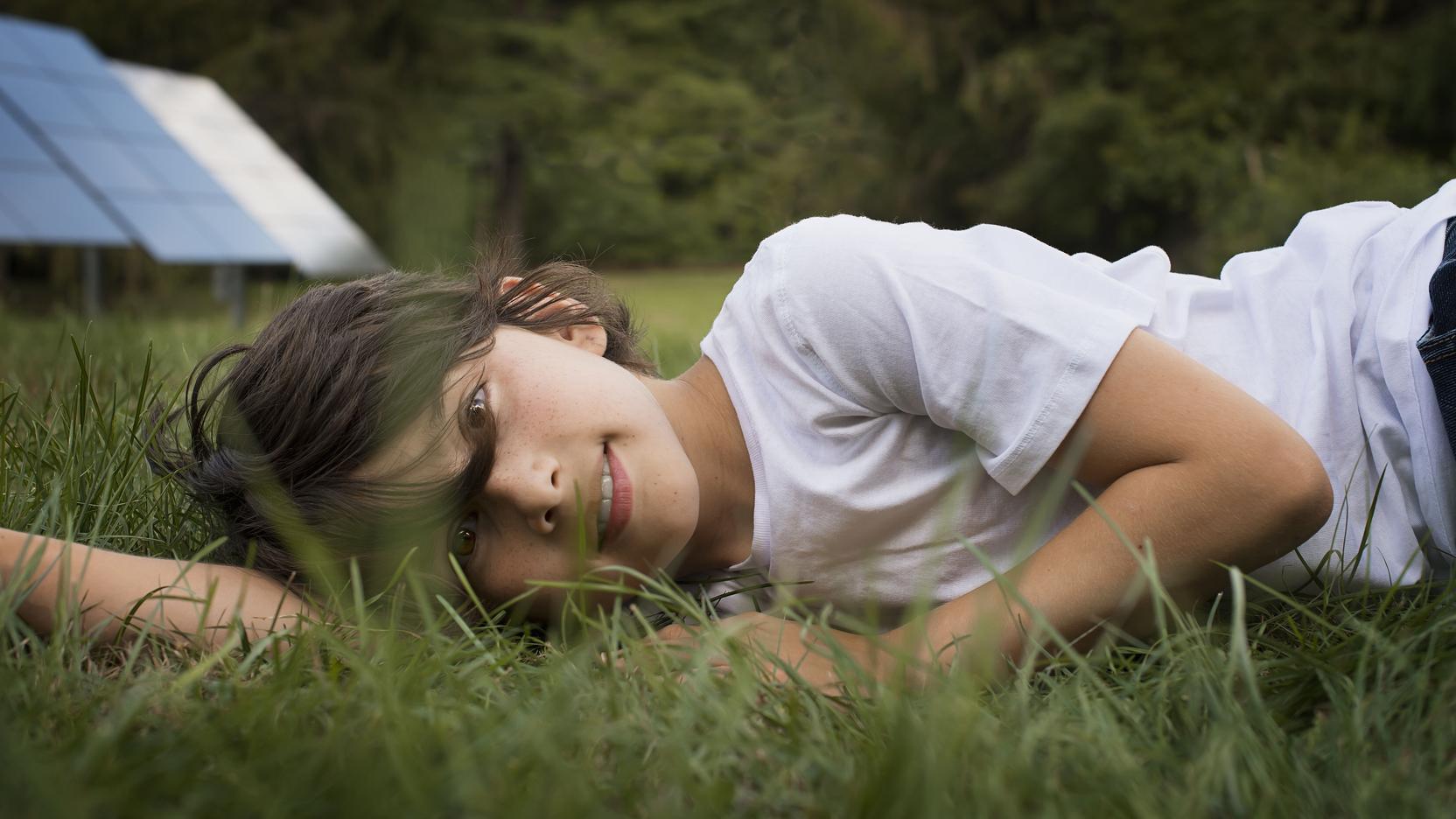 Ein Mädchen liegt auf einer grünen Wiese und grinst in die Kamera Ein Mädchen liegt auf einer grünen Wiese und grinst in die Kamera