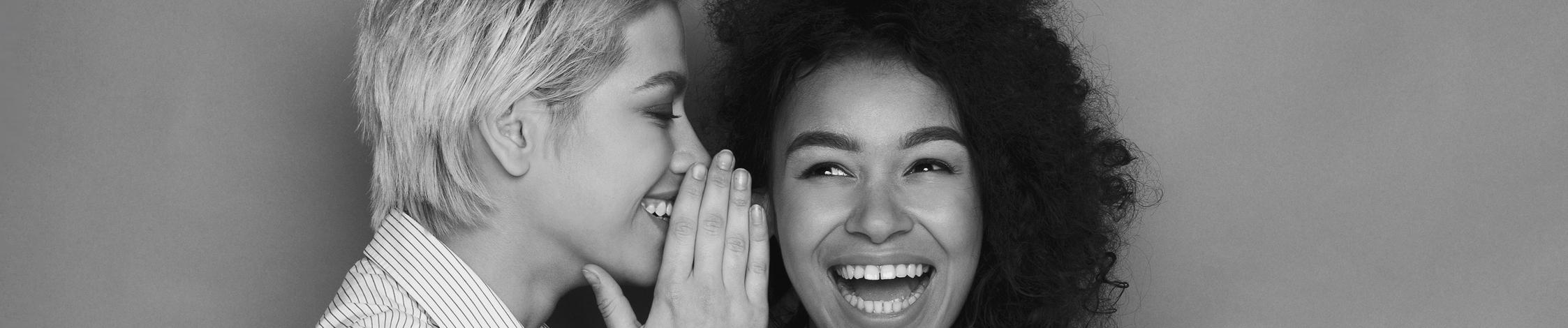 Eine Frau flüstert einer anderen Frau etwas zu